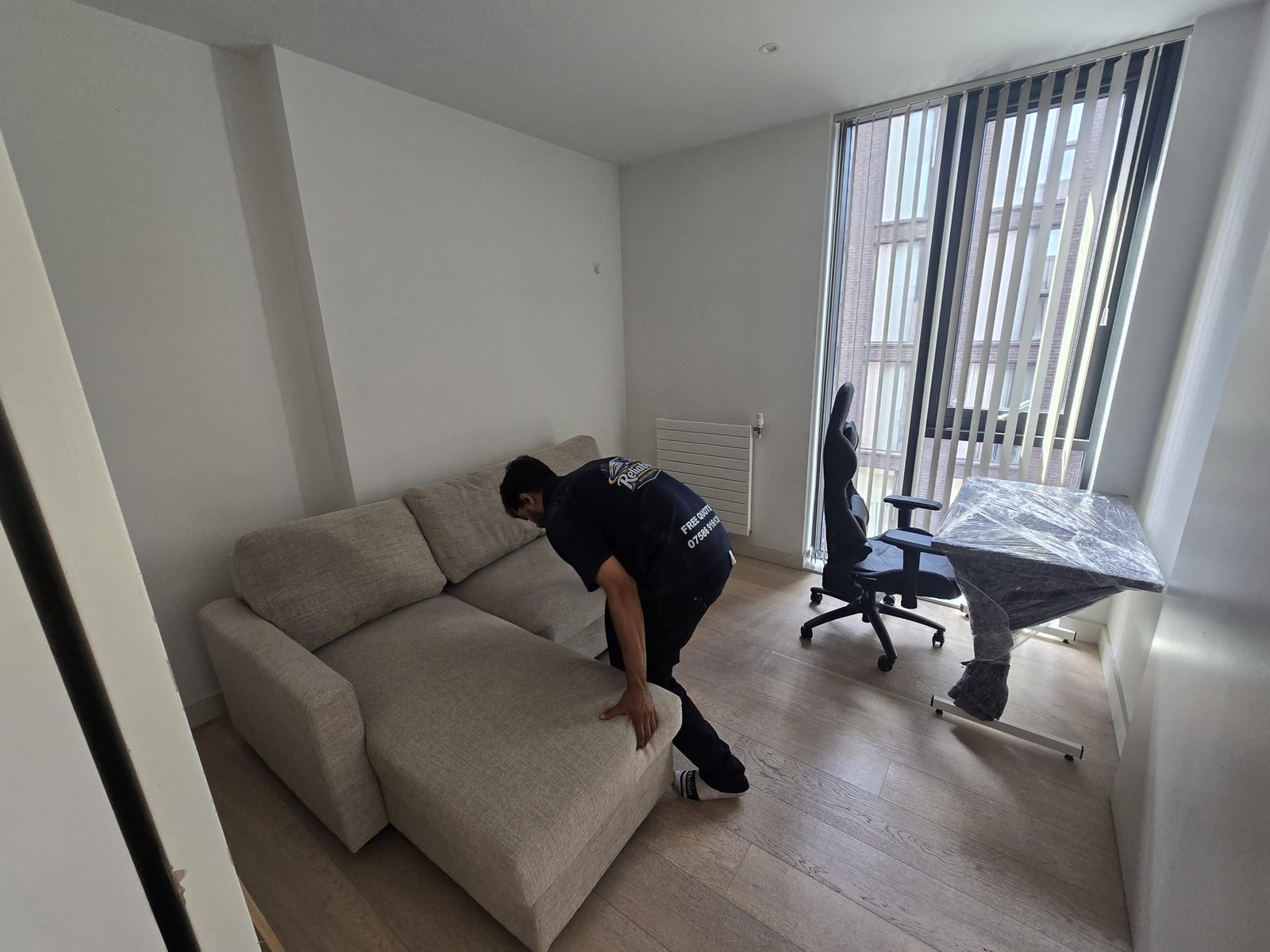 Mover placing a sofa in position in a bright Kingston flat after the move