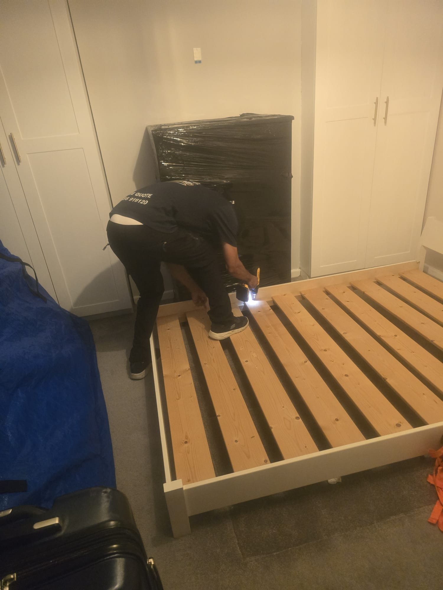 Bed frame being rebuilt next to a wrapped wardrobe in a Kingston bedroom